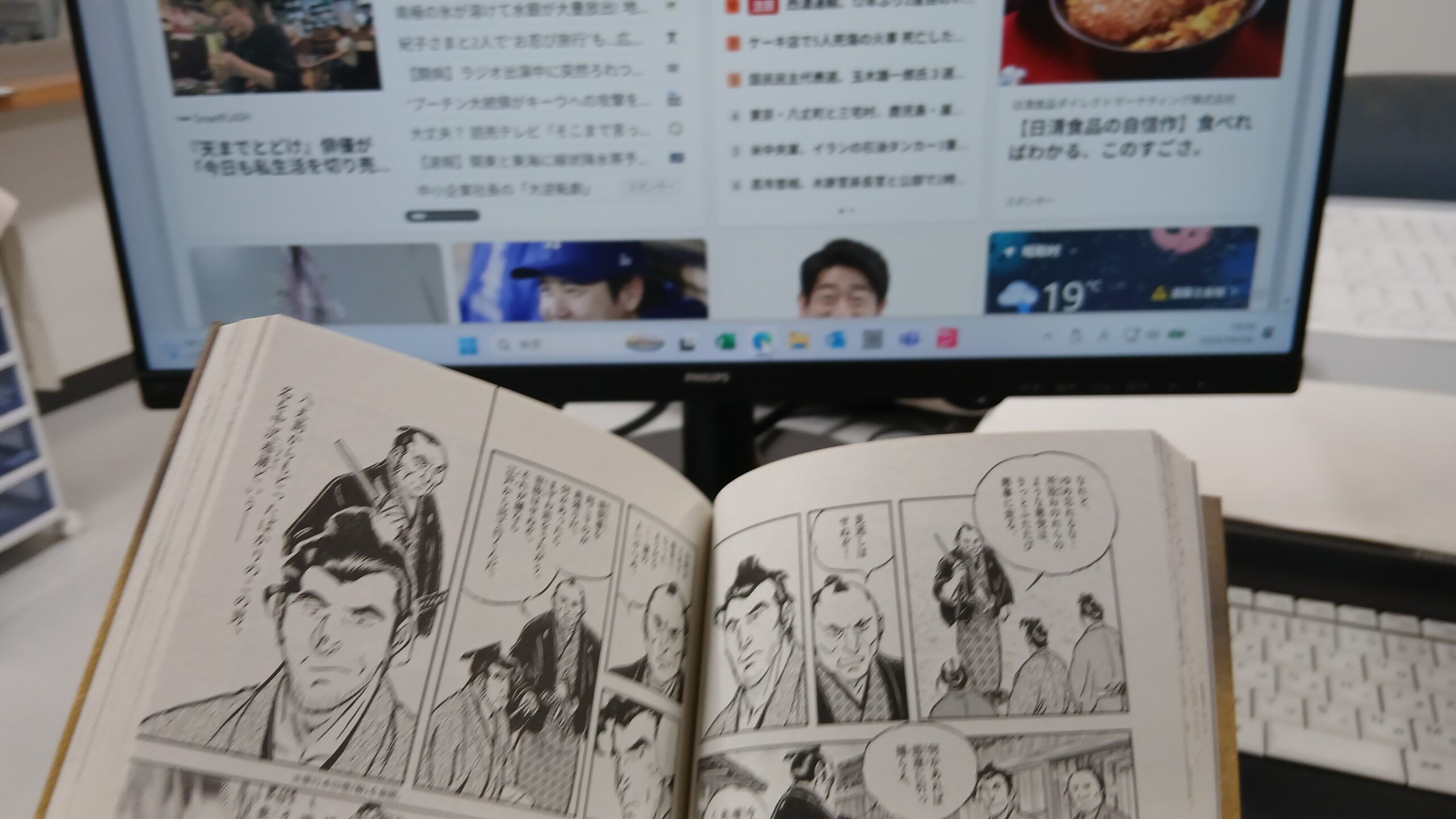 パソコンで情報を確認しながら紙の漫画を開いて読んでいる様子